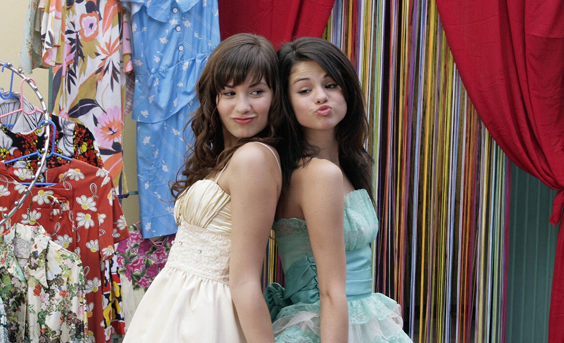 Demi Lovato and Selena Gomez posing with their backs against each other.